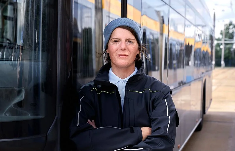 Die Busfahrerin Angela Rossberg steht mit vor dem Oberkörper verschränkten Armen vor einem Bus und schaut selbstbewusst in die Kamera.