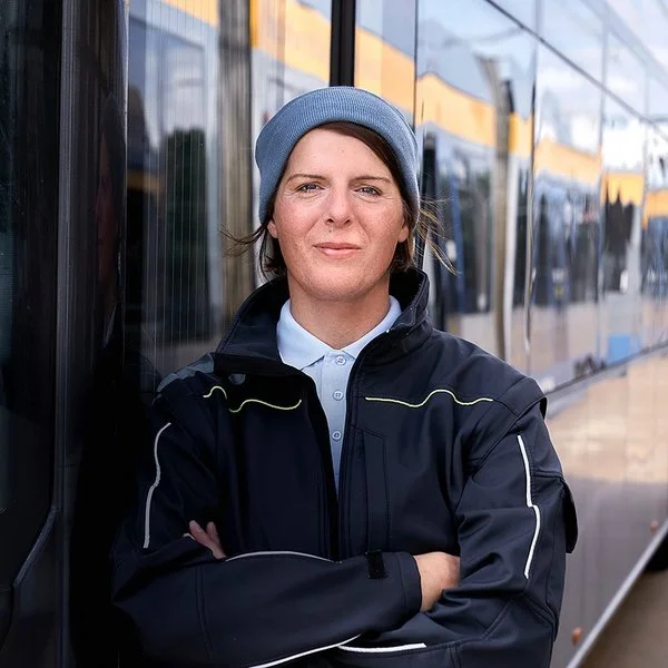 Die Busfahrerin Angela Rossberg steht mit vor dem Oberkörper verschränkten Armen vor einem Bus und schaut selbstbewusst in die Kamera.