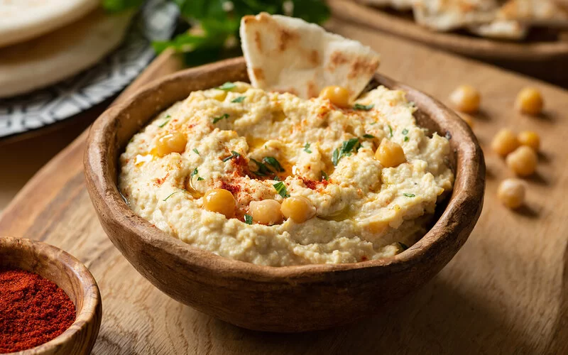 Hummus aus Kichererbsen in einer Holzschale angerichtet.