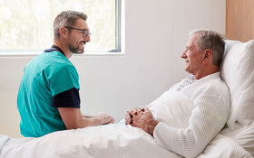 Ein Chirurg spricht mit einem Mann im Krankenbett über mögliche postoperative Schmerzen.