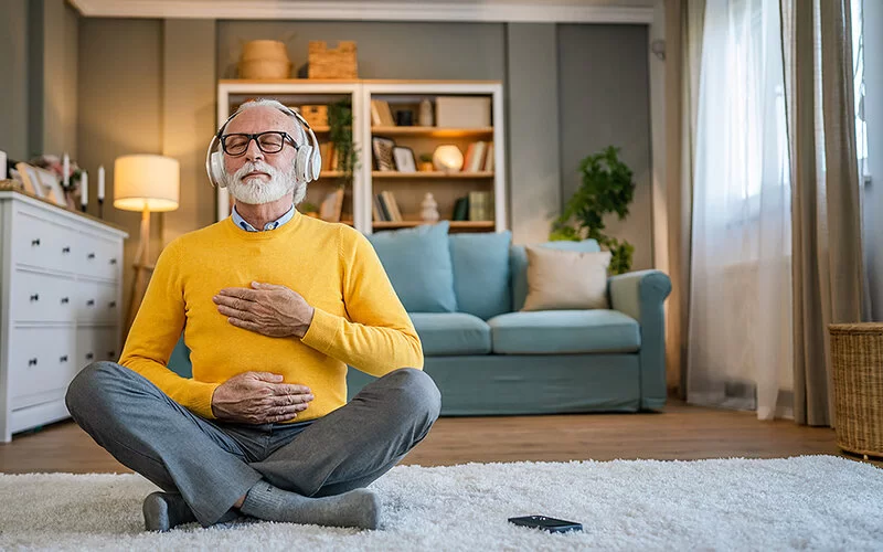 Ein älterer Mann meditiert auf dem Boden mit Kopfhörern, um seinen Reizmagen zu beruhigen.