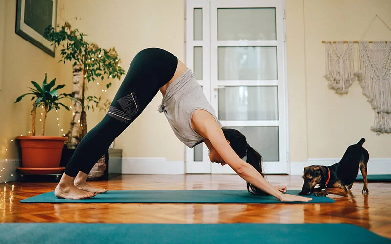 Eine Frau macht Yoga in ihrer Wohnung und befindet sich in der Position „Der herabschauende Hund“.