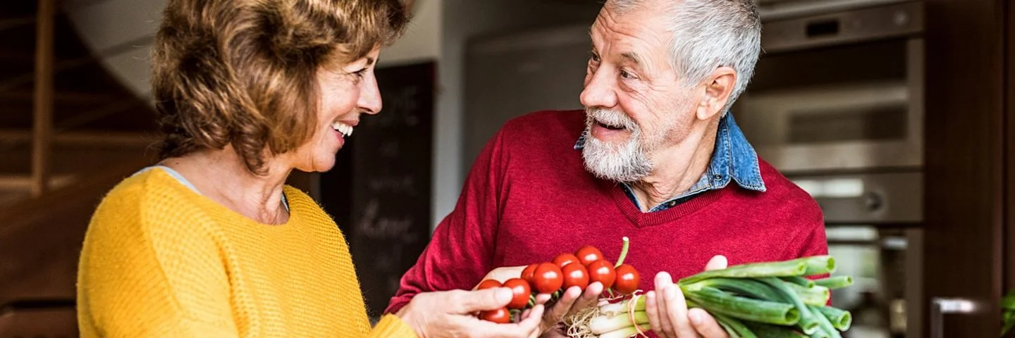 Ein älteres Paar packt Einkäufe aus, sie haben vor allem Gemüse gekauft.