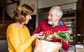 Ein älteres Paar packt Einkäufe aus, sie haben vor allem Gemüse gekauft.