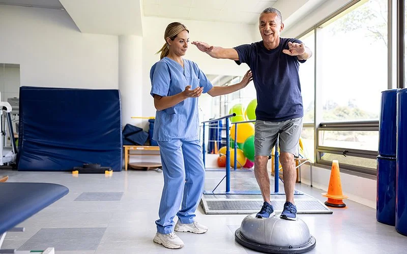 Ein Mann macht unter Anleitung einer Therapeutin Balance-Übungen.