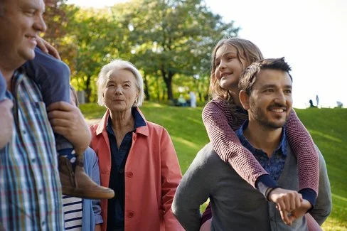 Eine Familie geht entspannt durch den Park. Die kommunale Gesundheitsförderung kann für Erholungsgebiete sorgen.