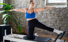 Eine Frau mit ausgestreckten Armen kniet auf einem Reformer.