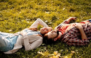 Situationship: Ein junger Mann und eine junge Frau liegen im Sonnenschein auf einer Wiese.