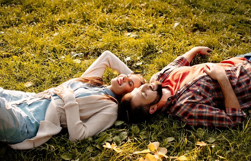 Situationship: Ein junger Mann und eine junge Frau liegen im Sonnenschein auf einer Wiese.