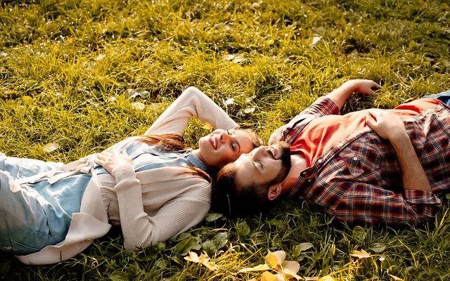 Situationship: Ein junger Mann und eine junge Frau liegen im Sonnenschein auf einer Wiese.