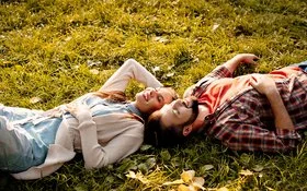 Situationship: Ein junger Mann und eine junge Frau liegen im Sonnenschein auf einer Wiese.