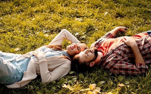 Situationship: Ein junger Mann und eine junge Frau liegen im Sonnenschein auf einer Wiese.