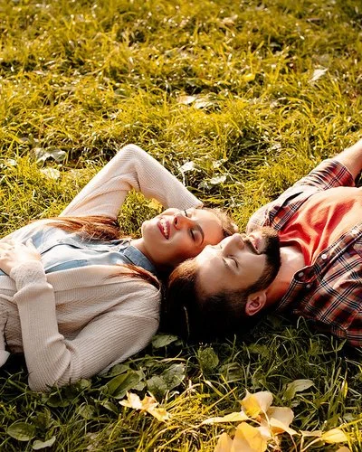 Situationship: Ein junger Mann und eine junge Frau liegen im Sonnenschein auf einer Wiese.