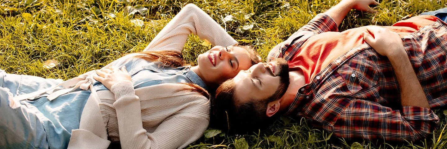 Situationship: Ein junger Mann und eine junge Frau liegen im Sonnenschein auf einer Wiese.