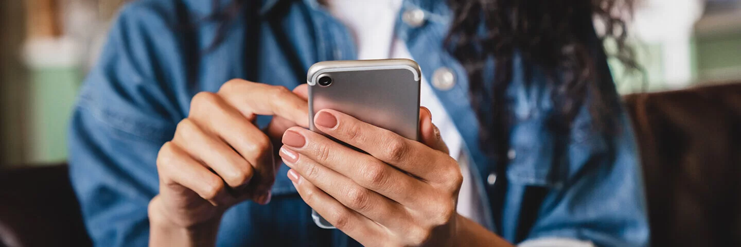 Eine junge Frau betrachtet ihr Smartphone. Die AOK bietet ihr die Möglichkeit einer elektronischen Patientenakte.