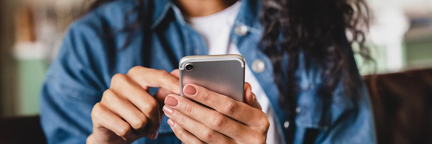 Eine junge Frau betrachtet ihr Smartphone. Die AOK bietet ihr die Möglichkeit einer elektronischen Patientenakte.