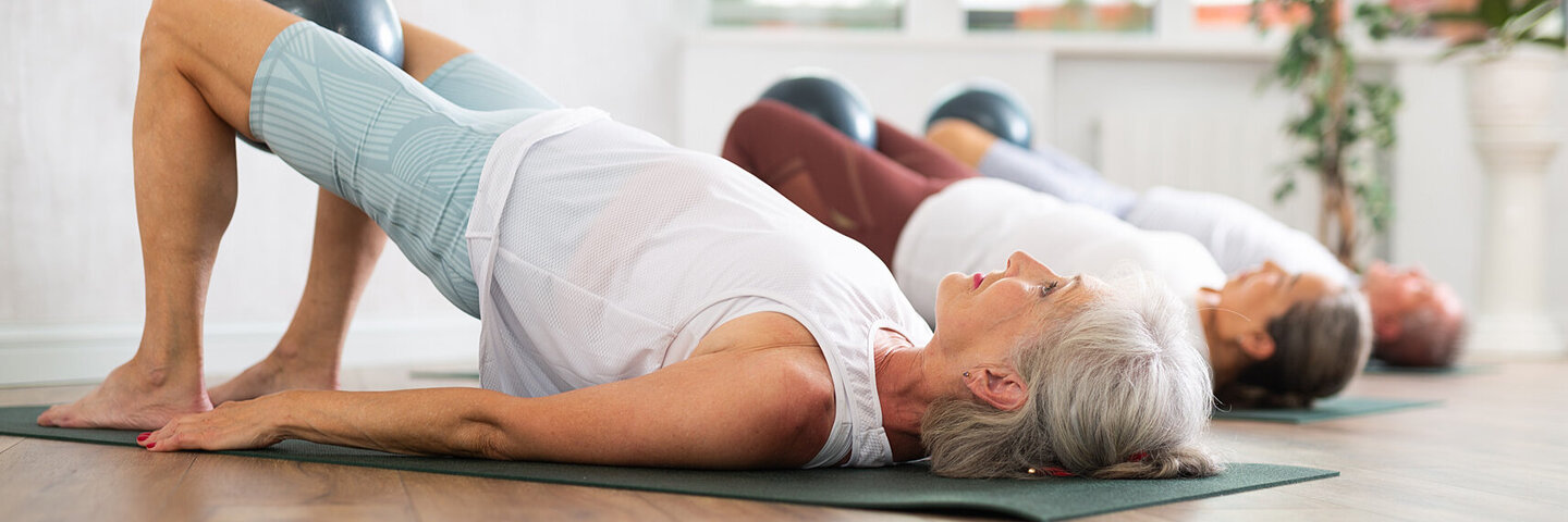 Eine Gruppe älterer Frauen turnt auf Yogamatten die Position „die Brücke“.