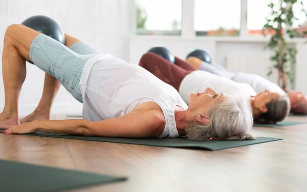 Eine Gruppe älterer Frauen turnt auf Yogamatten die Position „die Brücke“.