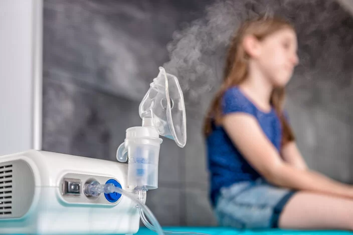 Ein junges Mädchen sitzt neben einem eingeschalteten Inhalationsgerät.