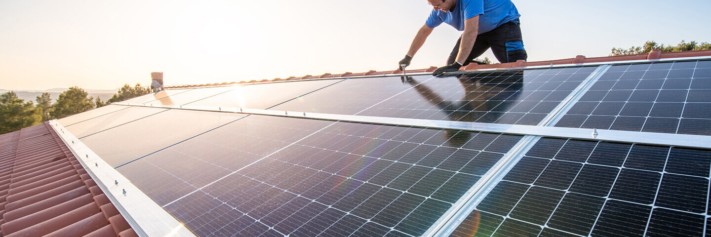 Ein Mann sitzt auf einem Dach und installiert eine Solaranlage.