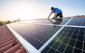 Ein Mann sitzt auf einem Dach und installiert eine Solaranlage.