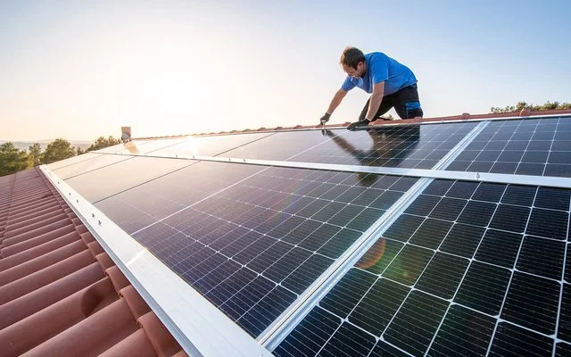 Ein Mann sitzt auf einem Dach und installiert eine Solaranlage.