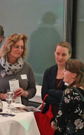 Eine Gruppe von Menschen steht um einen Tisch und unterhält sich.