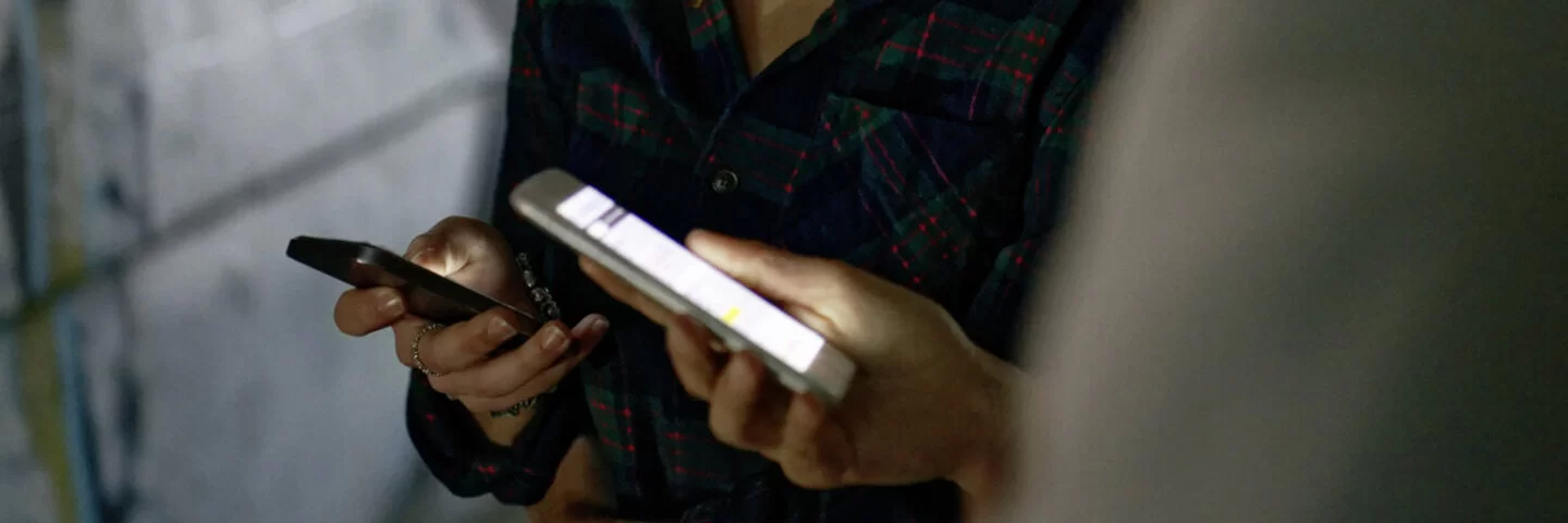 Ein Mädchen und ein Junge checken ihre Smartphones. Sie lächeln dabei in Richtung Display.