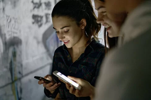 Ein Mädchen und ein Junge checken ihre Smartphones. Sie lächeln dabei in Richtung Display.