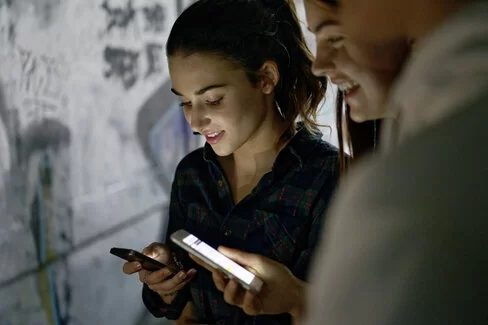 Ein Mädchen und ein Junge checken ihre Smartphones. Sie lächeln dabei in Richtung Display.