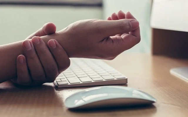 Jemand hält sich das Handgelenk wegen einem schmerzenden Mausarm-Syndrom.