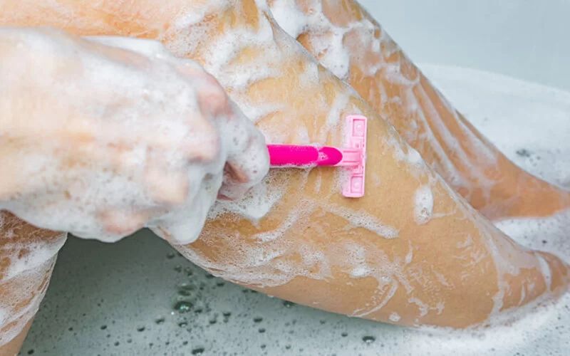 Eine Frau rasiert sich in der Badewanne die Beinhaare mit einem Einwegrasierer.