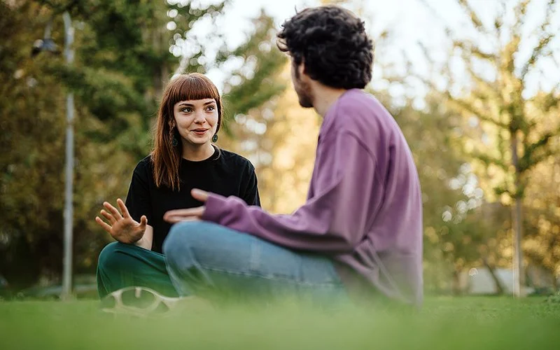Eine junge Frau und ein junger Mann sitzen auf einer Wiese und unterhalten sich über ihre Situationship.