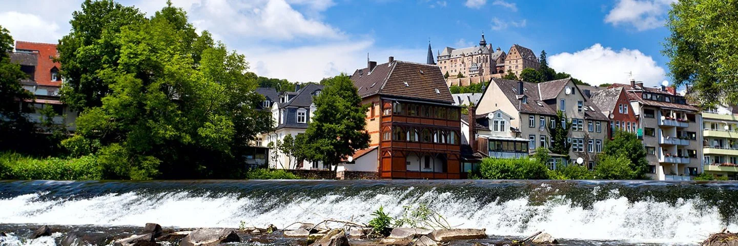 Marburg mit der Lahn im Vorder- und Schloss Marburg im Hintergrund.