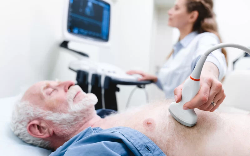 Eine Kardiologin führt eine Echokardiographie bei einem Patienten durch.