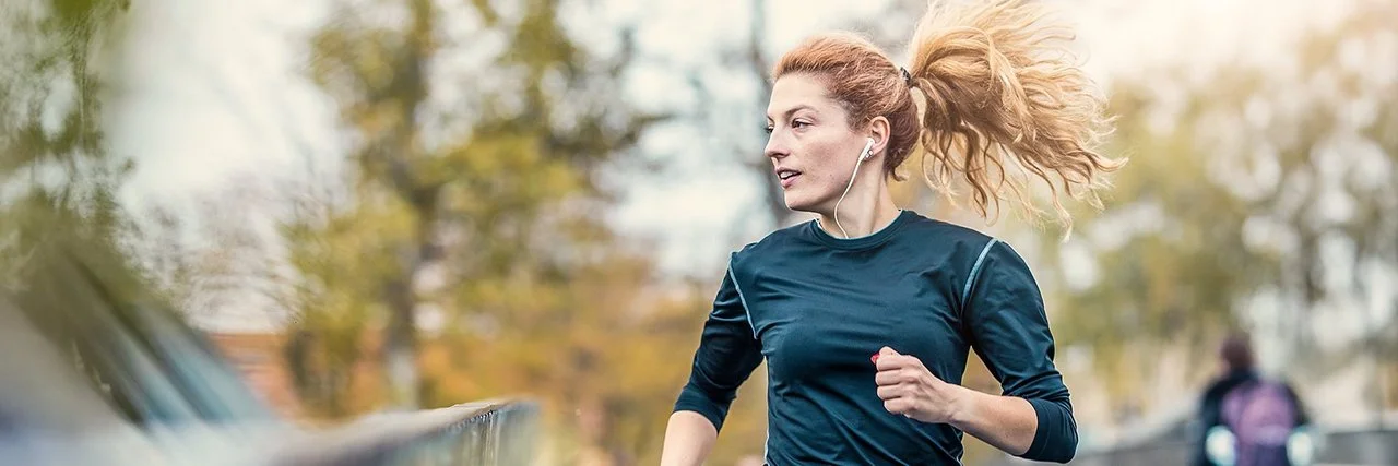 Eine junge Frau joggt über eine Brücke und hört dabei Musik.