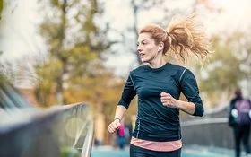 Eine junge Frau joggt über eine Brücke und hört dabei Musik.