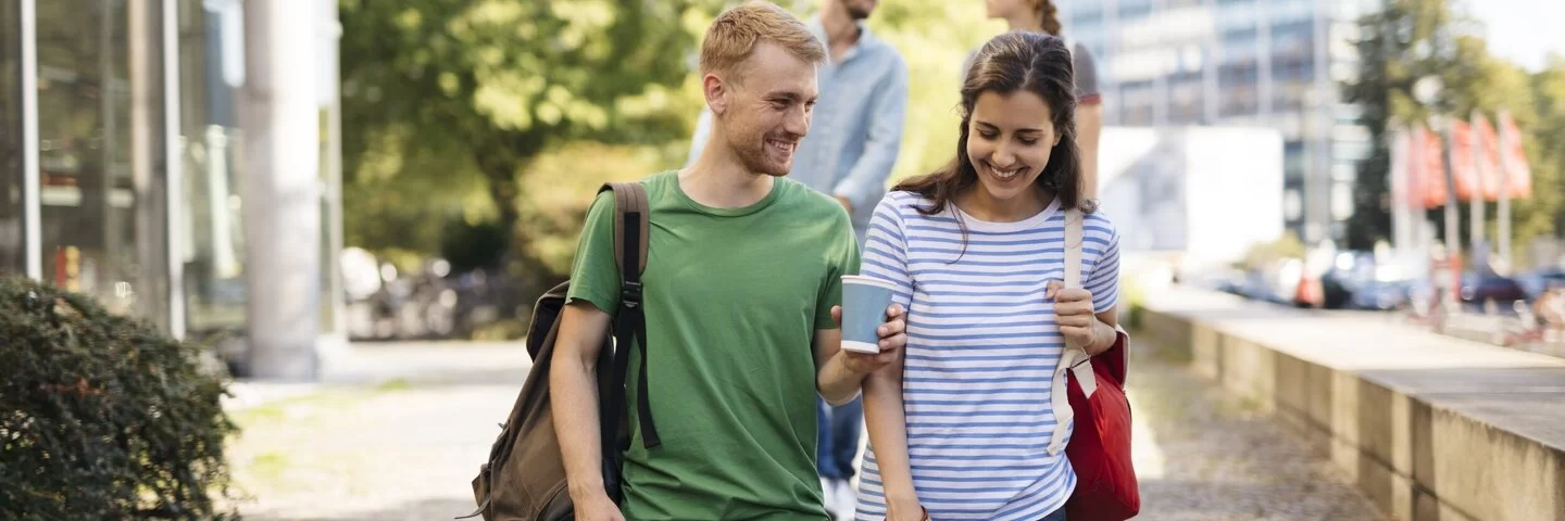 Junger Student und junge Studentin reden miteinander. Er hält ein Kaffebecher in der Hand. Schönes Pärchen.