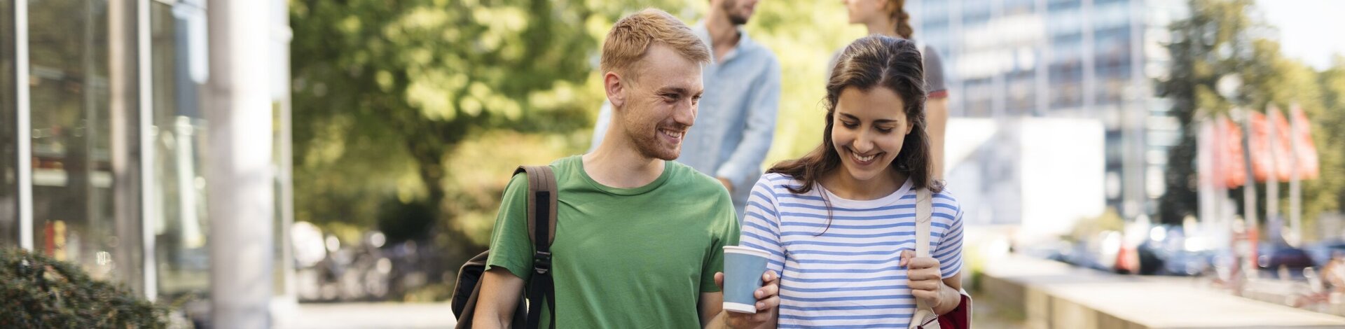 Junger Student und junge Studentin reden miteinander. Er hält ein Kaffebecher in der Hand. Schönes Pärchen.
