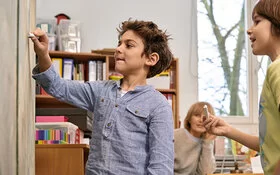 Ein Junge schreibt mit einem Stück Kreide etwas an eine Tafel. „Science Kids: Gesundheit entdecken“ regt den Entdeckergeist der Kinder in Sachen Gesundheit an.