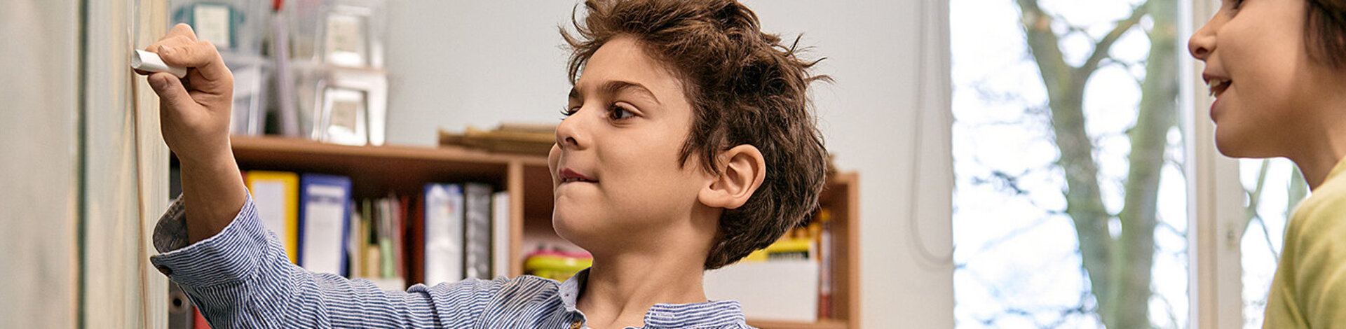 Ein Junge schreibt mit einem Stück Kreide etwas an eine Tafel. „Science Kids: Gesundheit entdecken“ regt den Entdeckergeist der Kinder in Sachen Gesundheit an.