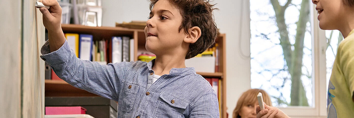 Ein Junge schreibt mit einem Stück Kreide etwas an eine Tafel. „Science Kids: Gesundheit entdecken“ regt den Entdeckergeist der Kinder in Sachen Gesundheit an.