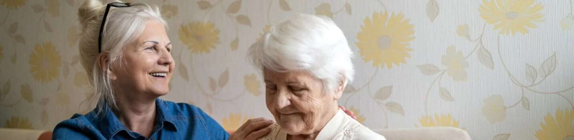 Frau hilft Seniorin sich in ihrem Schlafzimmer zu kleiden