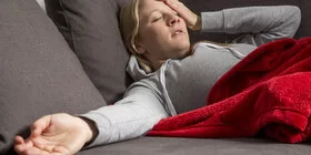 Eine Frau liegt auf dem Sofa und wirkt erschöpft.