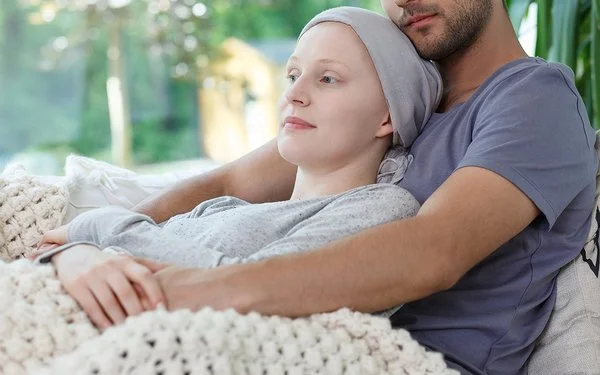 Ein Mann hält seine Frau, die eine Krebsbehandlung hatte und ihren Kopf mit einem Tuch bedeckt hat, liebevoll in den Armen.