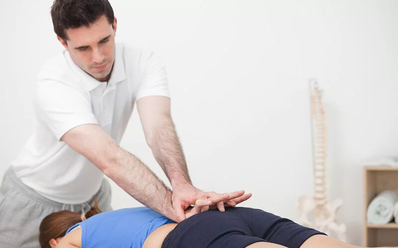 Physiotherapeut massiert eine auf dem Bauch liegende Patientin mit Steißbeinschmerzen am unteren Rücken.
