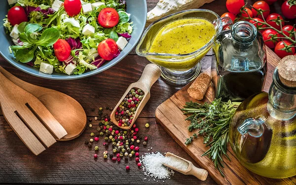 Eine große Schüssel mit gemischten Salat mitsamt einer frisch angemischten Vinaigrette und einer Essigflasche sowie Öl, Kräutern und Gewürzen.