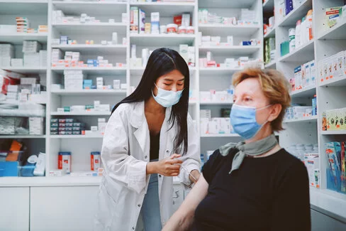Eine Ärztin gibt einer Frau eine Grippeschutzimpfung. Beide tragen Masken.