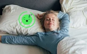 Eine blonde Frau liegt auf dem Rücken in ihrem Bett, die Augen geschlossen und streckt ihren Arm aus. 