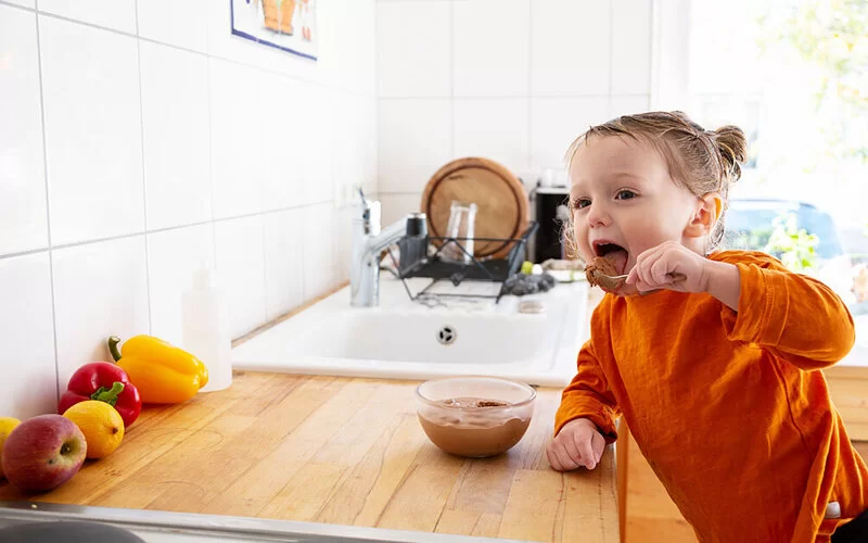 Kleines Kind isst in der Küche mit einem Löffel Schokoladencreme aus einer Schüssel.